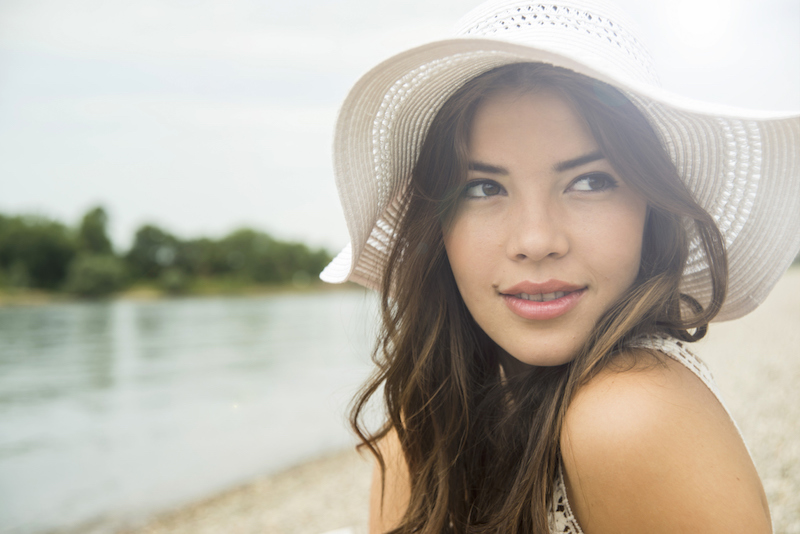 Portrait of young woman on the beach wearing white summer hat