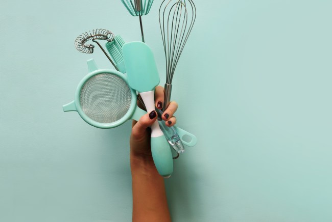 Model's hand holding blue cooking utensils.