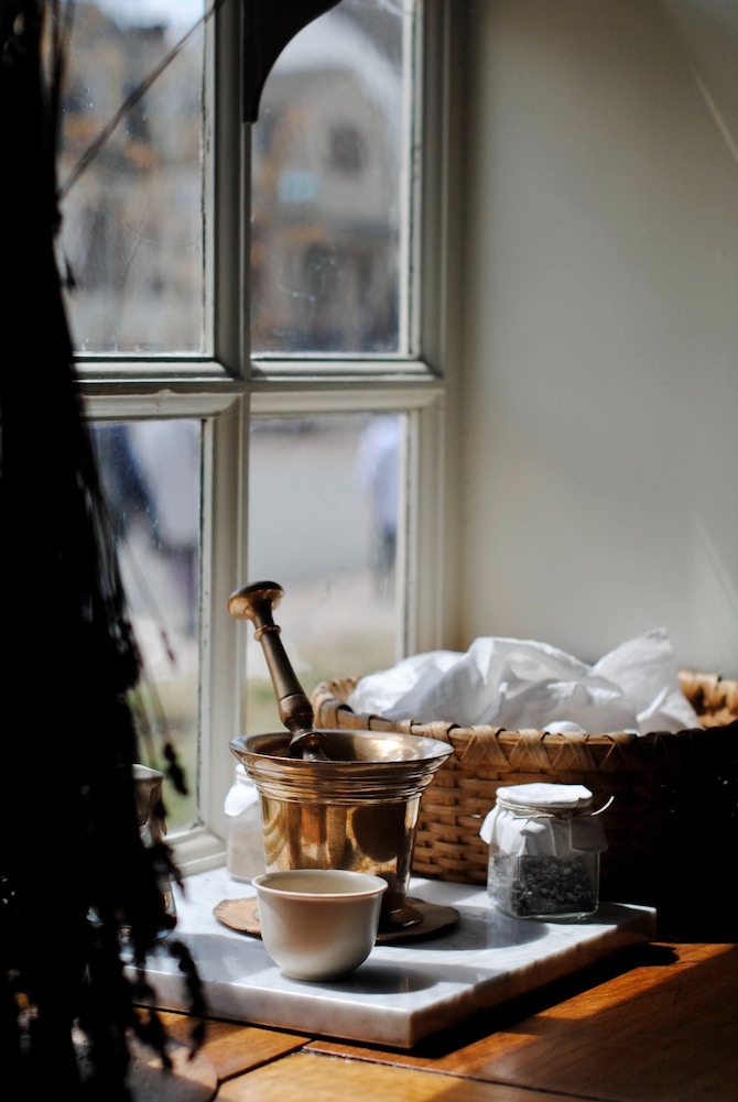 A windowsill decorated with a mortar and pestle, small ingredients, and a basket