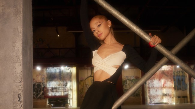 Ariana Grande holding on to scaffolding in a warehouse