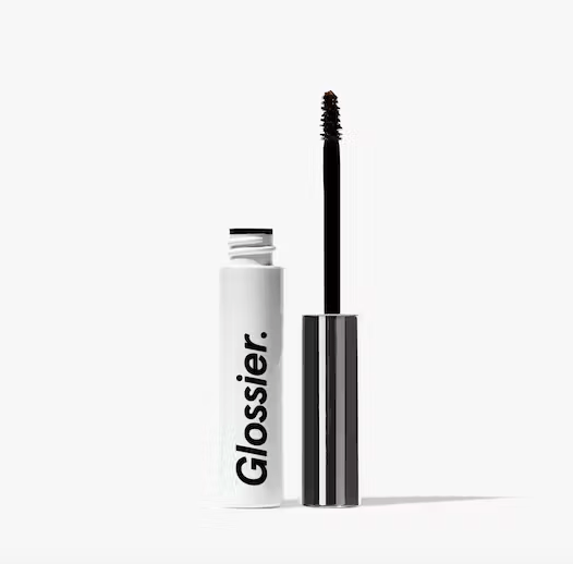 An open tube of Glossier Boy Brow, standing next to its brush