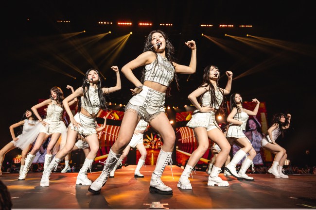 K-Pop Girl Group IVE, six Asian women ANYUJIN, GAEUL, REI, JANGWONYOUNG, LIZ, and LEESEO, dancing with white outfits on stage. 