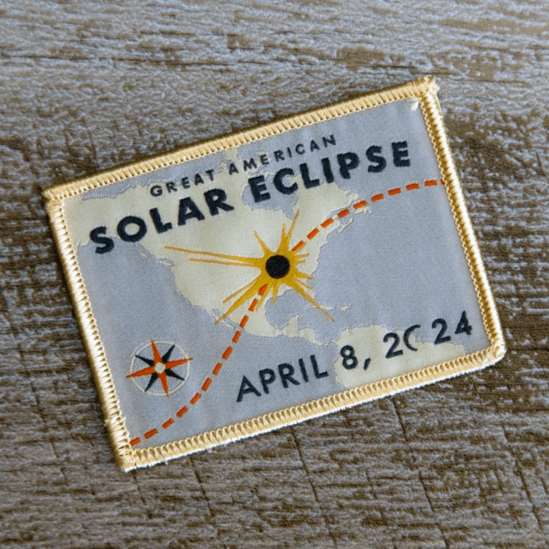 An iron-on patch that says "Great American Solar Eclipse April 8, 2024" and has a map of the U.S. with the eclipse path over it