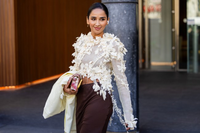 A street style star wearing a white, long-sleeve flower-covered blouse with brown pants at Paris Fashion Week
