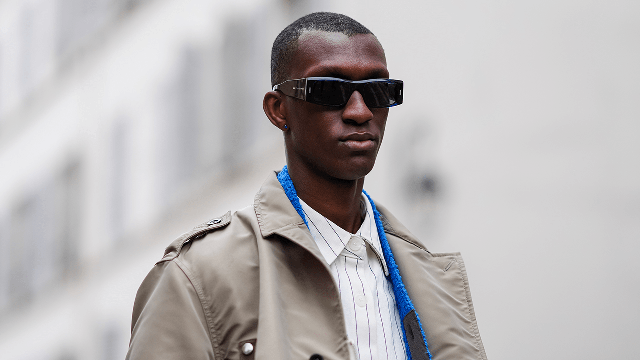 A guest wears sunglasses, a white shirt with stripes, a beige trench long coat , outside Sacai, during the Menswear Fall/Winter 2024/2025 as part of Paris Fashion Week on January 21, 2024 in Paris, France.