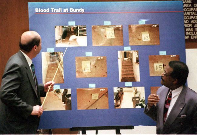Los Angeles Police Detective Tom Lange (L) points to pictures 06 March of the trail of blood at Nicole Brown Simpson's condominium where she and her friend Ron Goldman were murdered 12 June 1994 during testimony in the OJ Simpson murder trial.  Lange, one of the lead investigators in the case, was cross-examined by the defense as to his actions at the murder scene. On the right is Simpson attorney Johnnie   Cochran, Jr.