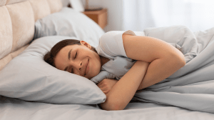Content woman hugging blanket and smiling in bed