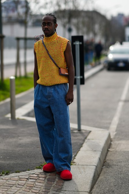 man poses for street style photographer in baggy jeans and a knit tank
