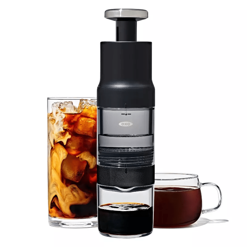 OXO BREW Rapid Brewer Single-Serve Coffee Maker in black next to a mug and a cup of coffee