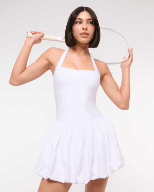 A model wearing the Abercrombie & Fitch YPB motionTEK Halter Bubble Hem Mini Dress in white