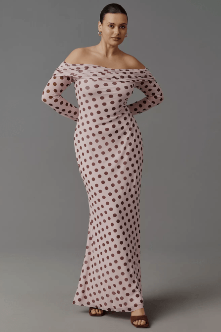 A plus-sizem model wearing the AFRM Long-Sleeve Off-The-Shoulder Mesh Maxi Dress in a light lilac and brown-black polka dot pattern