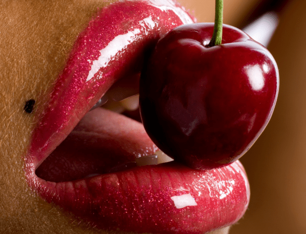 A cherry in between a woman's glossy lips