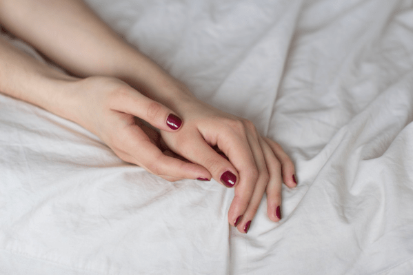 A woman's hands on top of bed sheets
