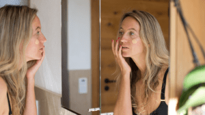 A woman applying foundations to her face with her finger in the bathroom mirror