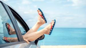 A car with a woman's feet hanging out of the window, in front of the beach
