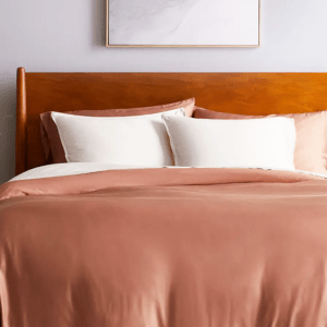 A bed covered in Quince's bamboo bedding in a soft salmon pink colorway with white pillows.