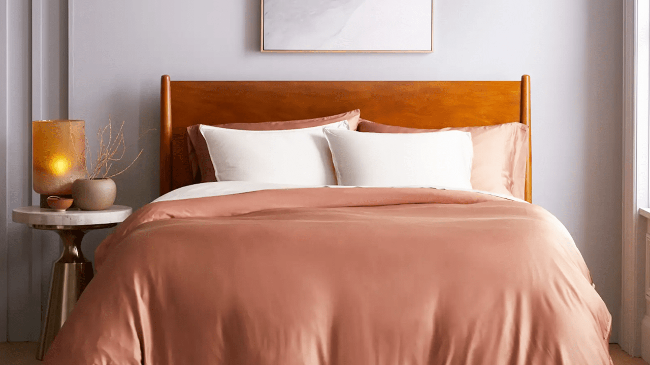 A bed covered in Quince's bamboo bedding in a soft salmon pink colorway with white pillows.